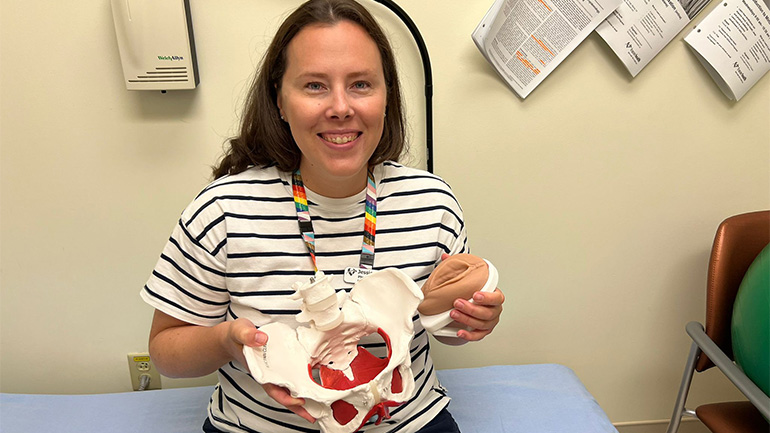 A woman holding a pelvic model and smiling