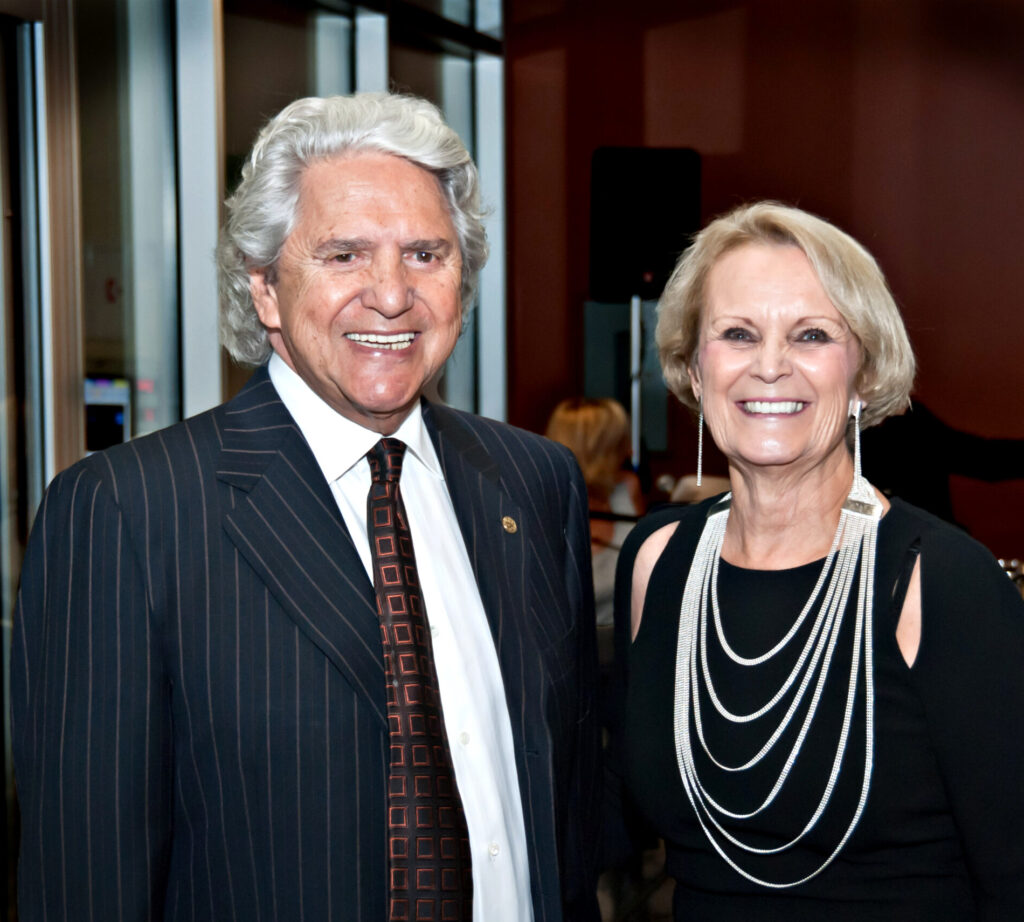 An older couple dressed in formal attire smiling at the camera at an indoor event. 